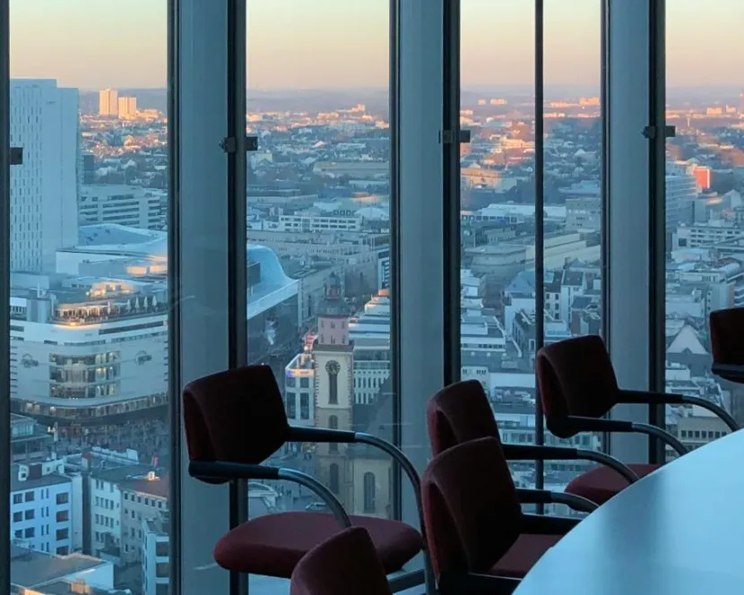 A boardroom with large glass windows and a dusky view of a city.