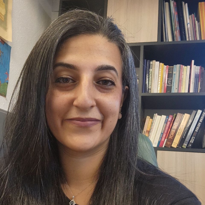 Layal Khatib sits in her office. Behind her is a bookshelf brimming wiht books.