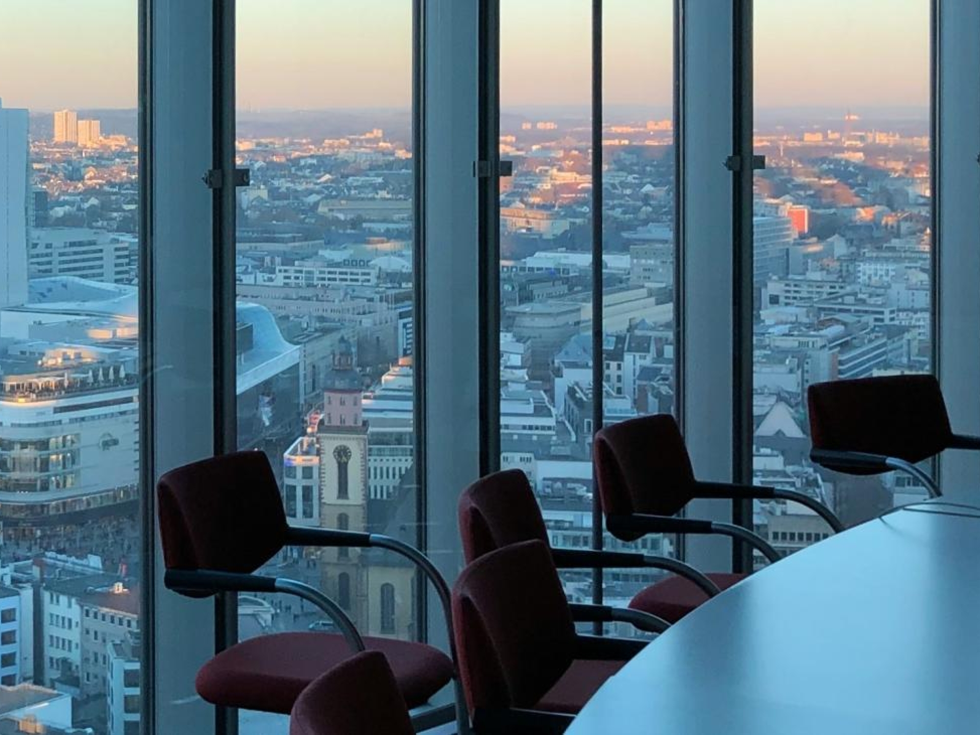 A boardroom with large glass windows and a dusky view of a city.